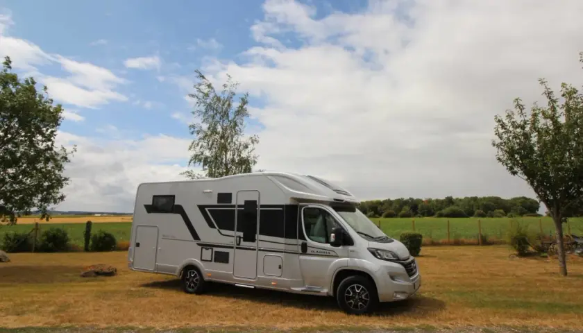 Camping-car Adria Matrix 670 SC argenté, stationné dans un champ sous un ciel nuageux.