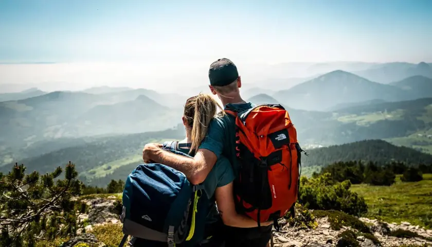 Couple en randonnée, admirant le panorama des montagnes de la Grande Ardèche. Sacs à dos orange et bleus, vue imprenable.