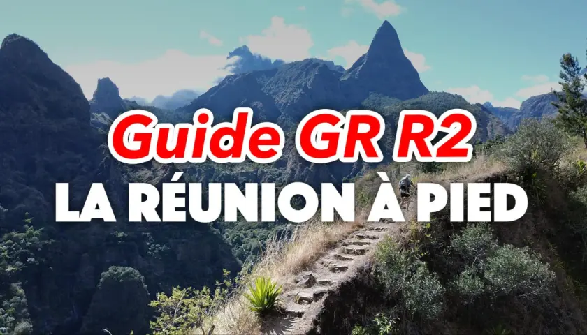 Guide GR R2 : La Réunion à pied, un randonneur sur un sentier escarpé avec des montagnes majestueuses en arrière-plan.