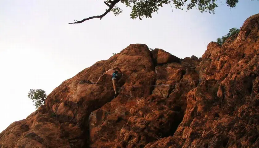 Escalade dans la gorge du Blavet, un grimpeur progresse sur une paroi rocheuse ocre sous un ciel clair.