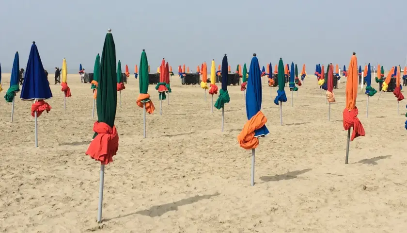 Des parasols colorés, bleus, verts, rouges et jaunes, sont alignés sur la plage de Deauville, prêts à accueillir les visiteurs.