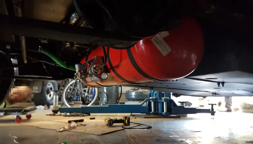 Installation d'un réservoir GPL sous un camping-car, respectant la réglementation GPL camping-car. Le réservoir rouge est visible, fixé sous le châssis.