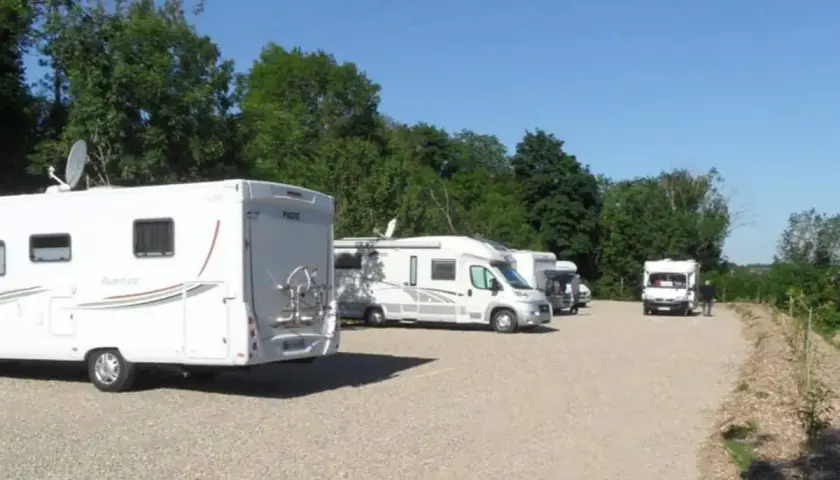 Stationnement de camping-cars sous un ciel bleu, avec des arbres en arrière-plan. Une aire camping car Arras paisible pour les voyageurs.