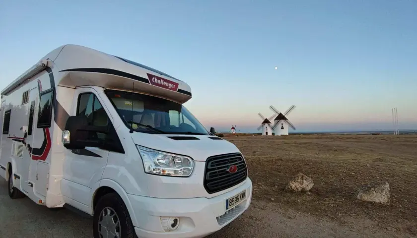Un camping-car blanc est garé devant des moulins à vent au coucher du soleil. Un voyage en camping-car inoubliable.