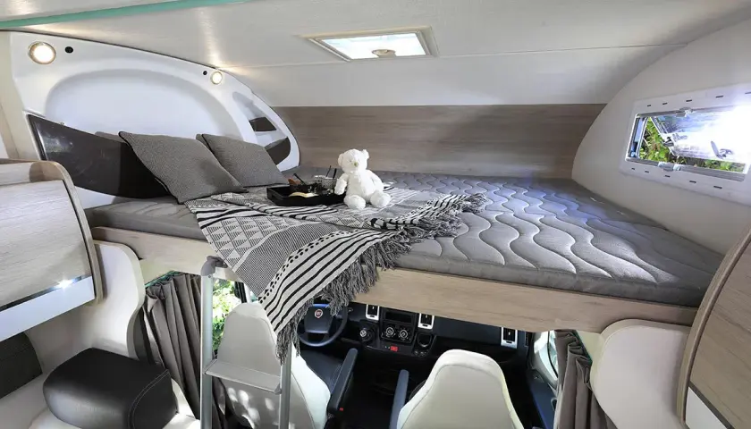 Lit pavillon confortable dans un camping-car, prêt pour une nuit paisible. Un ours en peluche veille sur le sommeil.