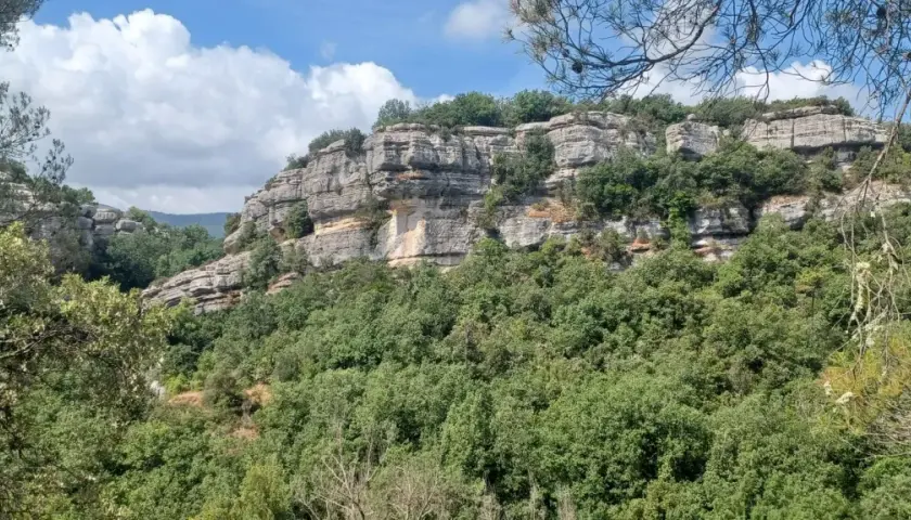 Falaises calcaires spectaculaires des gorges du Caramy, couvertes de végétation luxuriante sous un ciel bleu et nuageux.