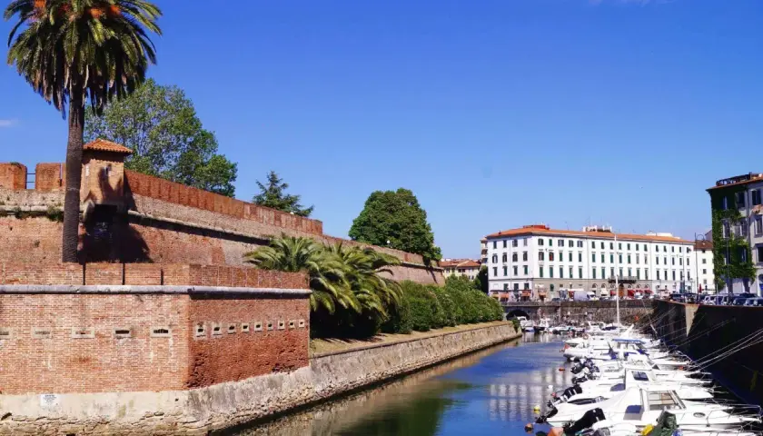Canal bordé de bateaux à Livourne, Italie, avec une ancienne muraille de briques et des palmiers.