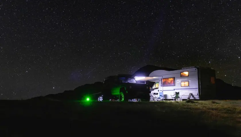 Un camping-car et un 4x4 illuminés sous un ciel étoilé. L'endroit parfait où dormir en camping-car pour admirer la voie lactée.