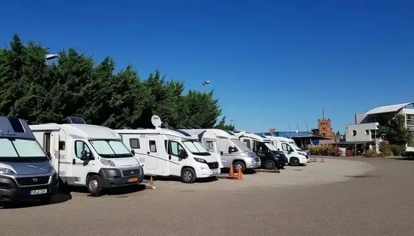 Rangée de camping-cars blancs et gris garés sous un ciel bleu clair.