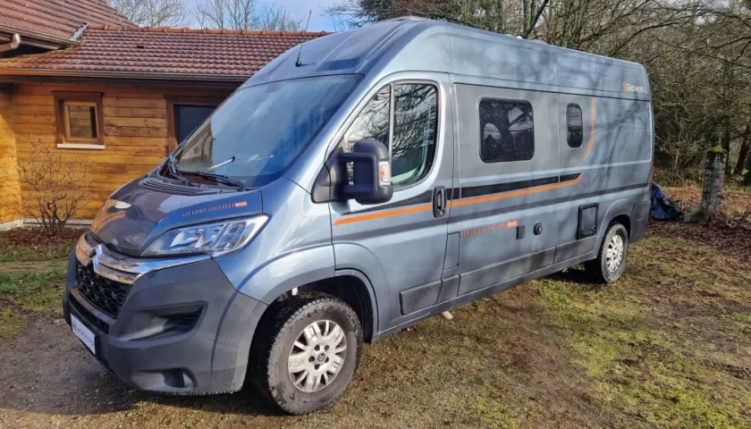 Un camping-car gris, modèle Globecar, est garé devant une maison en bois. Il est prêt pour une aventure avec son look d'Argus.