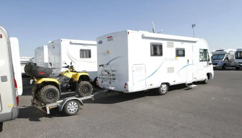 Un quad jaune sur une remorque, prêt à être tracté par un camping-car. Le quad est bien attaché, prêt pour l'aventure, comme indiqué sur la carte grise.