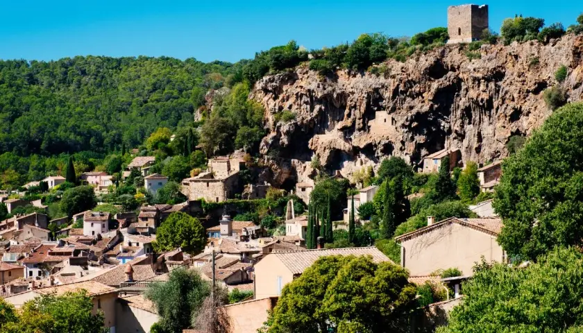 Vue d'un village perché du Var, accroché à une falaise rocheuse, avec des maisons aux toits de tuiles et une tour médiévale.