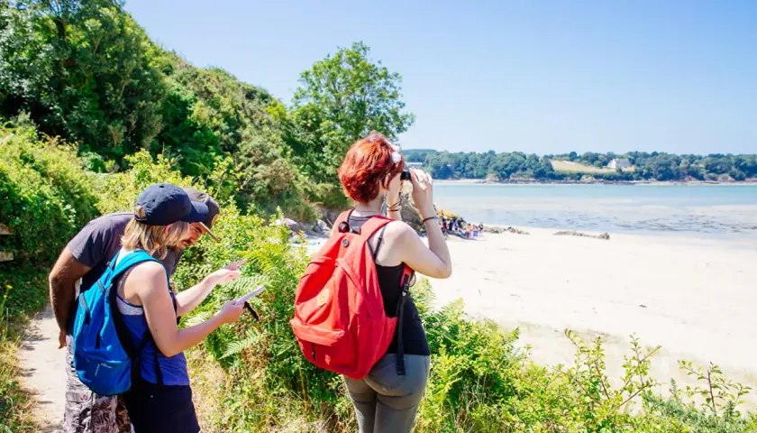 Couple en randonnée à Saint-Jacut-de-la-Mer, consultant une carte. Une femme observe la baie avec des jumelles.