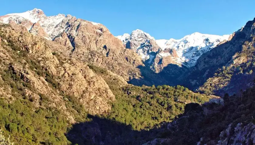 Vue spectaculaire de **mare e monti** : des montagnes enneigées surplombent une vallée verdoyante, avec un soleil éclatant illuminant le paysage.