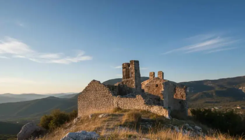 Ruines d'un château médiéval à Châteauneuf-les-Moustiers, baignées par la lumière dorée du soleil couchant, dominant un paysage de collines verdoyantes.