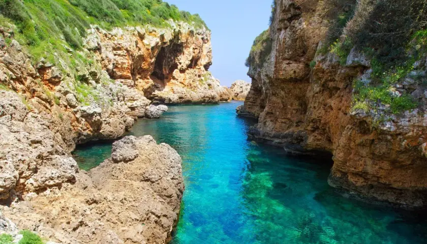 Magnifique paysage minorquin : criques rocheuses aux eaux turquoise cristallines, végétation luxuriante sur les falaises.