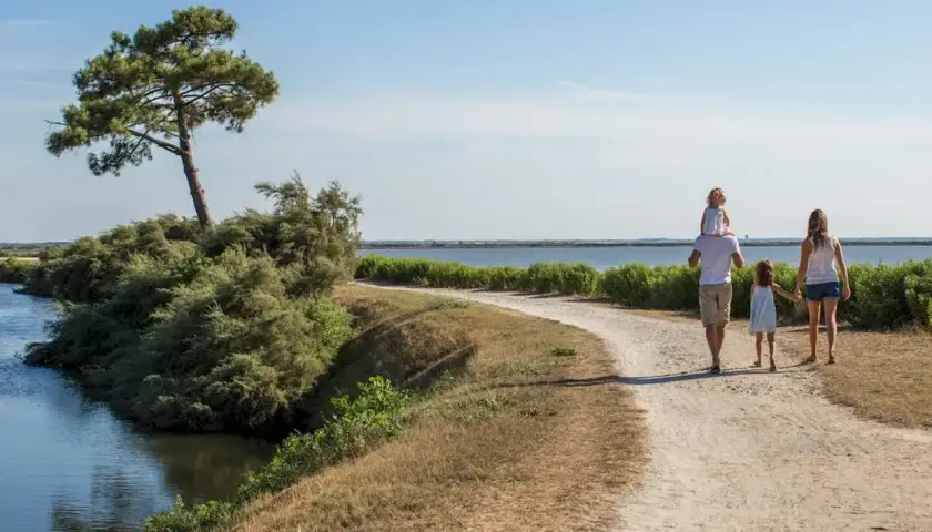 Une famille profite d'une randonnée à Arcachon, longeant un cours d'eau sous un ciel bleu.