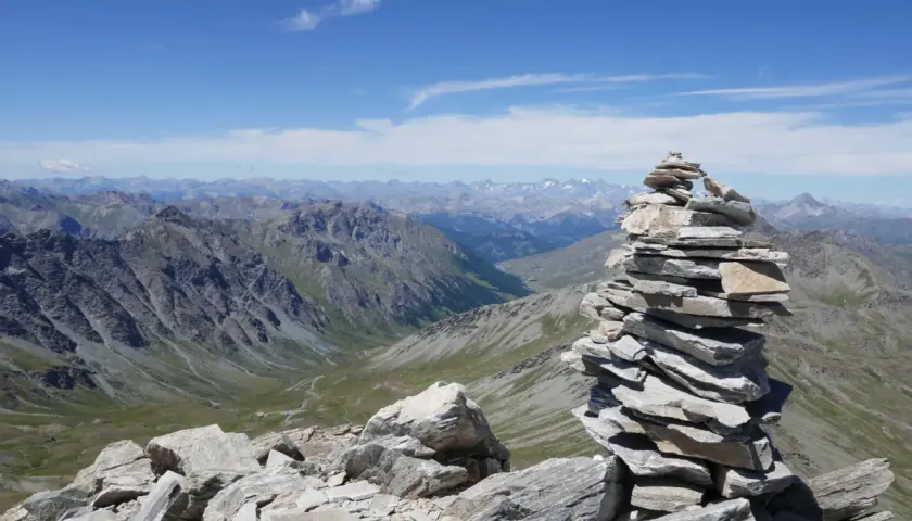 Un cairn, tel un tour du pain de sucre, domine un paysage de montagnes majestueuses sous un ciel bleu.