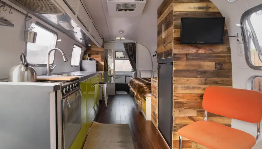 Intérieur d'une caravane Airstream rénovée, avec cuisine, lit douillet et mur en bois rustique.