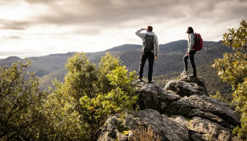 Deux randonneurs contemplent un paysage montagneux depuis un promontoire rocheux, profitant d'une vue panoramique.