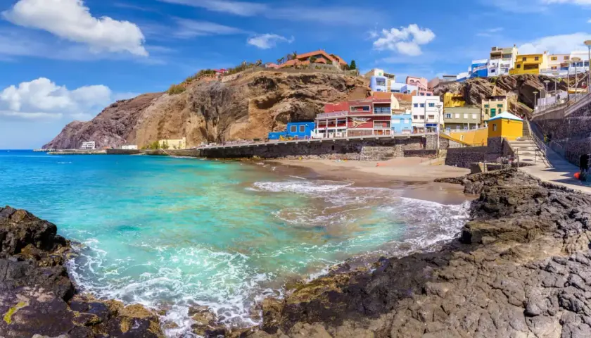 Plage de sable, maisons colorées accrochées à flanc de falaise, eaux turquoise. Idéal pour savoir que faire aux Canaries.