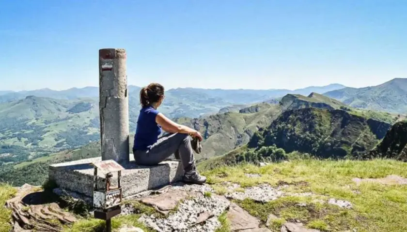 Vue panoramique sur les montagnes verdoyantes du gr pays basque. Une randonneuse contemple le paysage depuis un sommet.