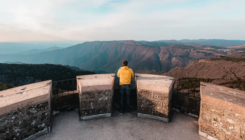 Un homme en jaune admire le panorama depuis le sommet du mont Aigoual, avec ses vastes étendues de montagnes bleues à perte de vue.