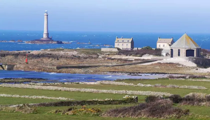Vue panoramique de la Pointe de la Hague avec son phare emblématique, des maisons de pierre et des champs verdoyants.