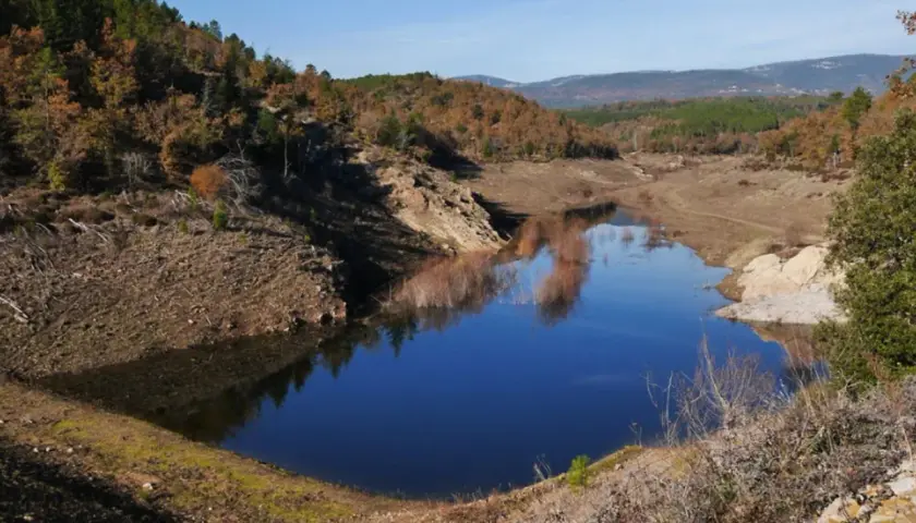 Le lac de Meaulx, aux reflets bleus intenses, est entouré de collines boisées aux couleurs d'automne.