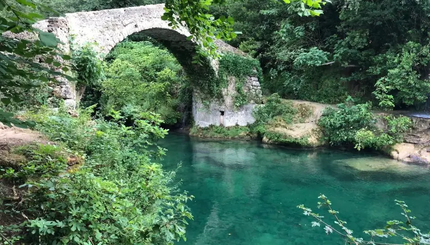Un pont de pierre enjambe les eaux turquoise des gorges de la Siagne, entouré d'une végétation luxuriante.