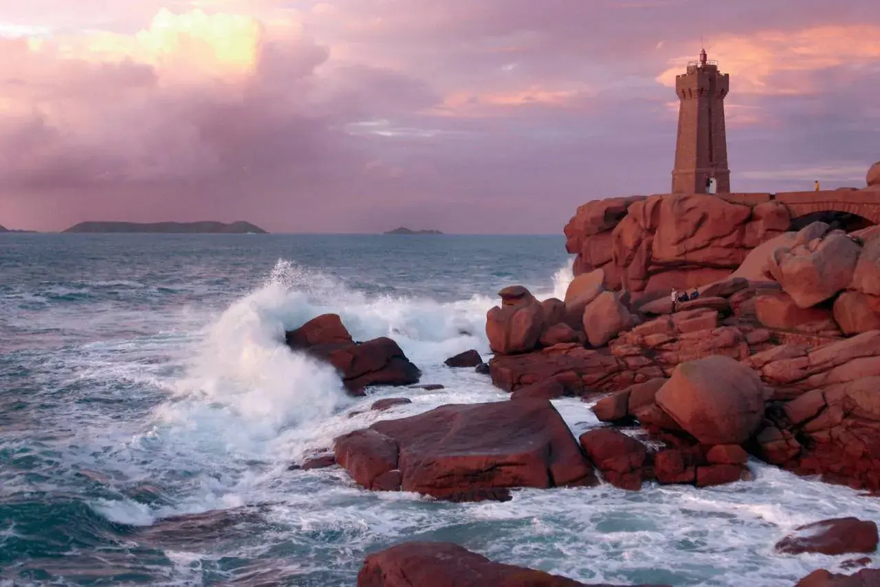 Phare de Ploumanac'h, un joyau pour visiter la Bretagne. Vagues s'écrasant sur les rochers roses sous un ciel pastel.