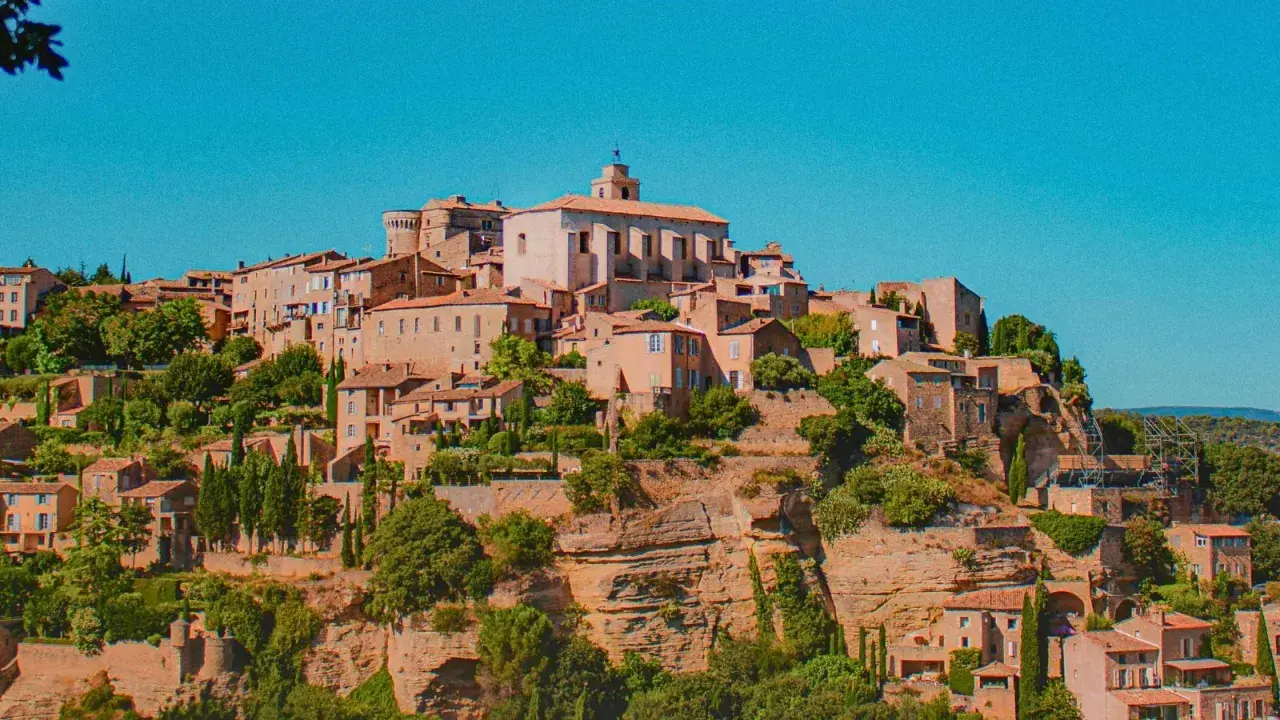 Village perché en Provence, idéal pour un budget vacances. Maisons en pierre, toits de tuiles, végétation luxuriante sous un ciel bleu.