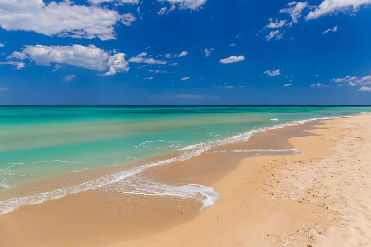 Plage de Bari, sable doré, eaux turquoise et ciel bleu azur avec des nuages blancs. Un rêve d'évasion.