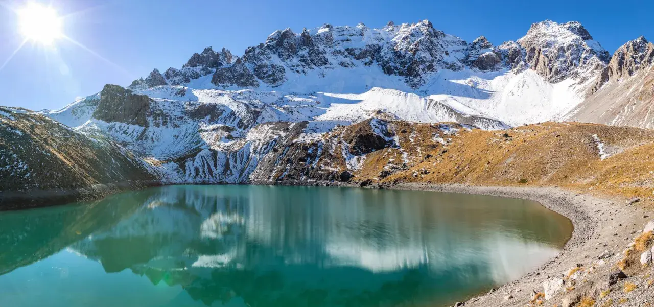 Lac d'altitude aux eaux turquoise, reflets des montagnes enneigées. Idéal pour une randonnée à Ceillac par temps ensoleillé.