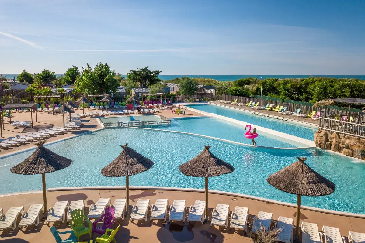 Belle aire camping car à Marseillan avec piscines, transats et parasols. La mer est visible au loin.