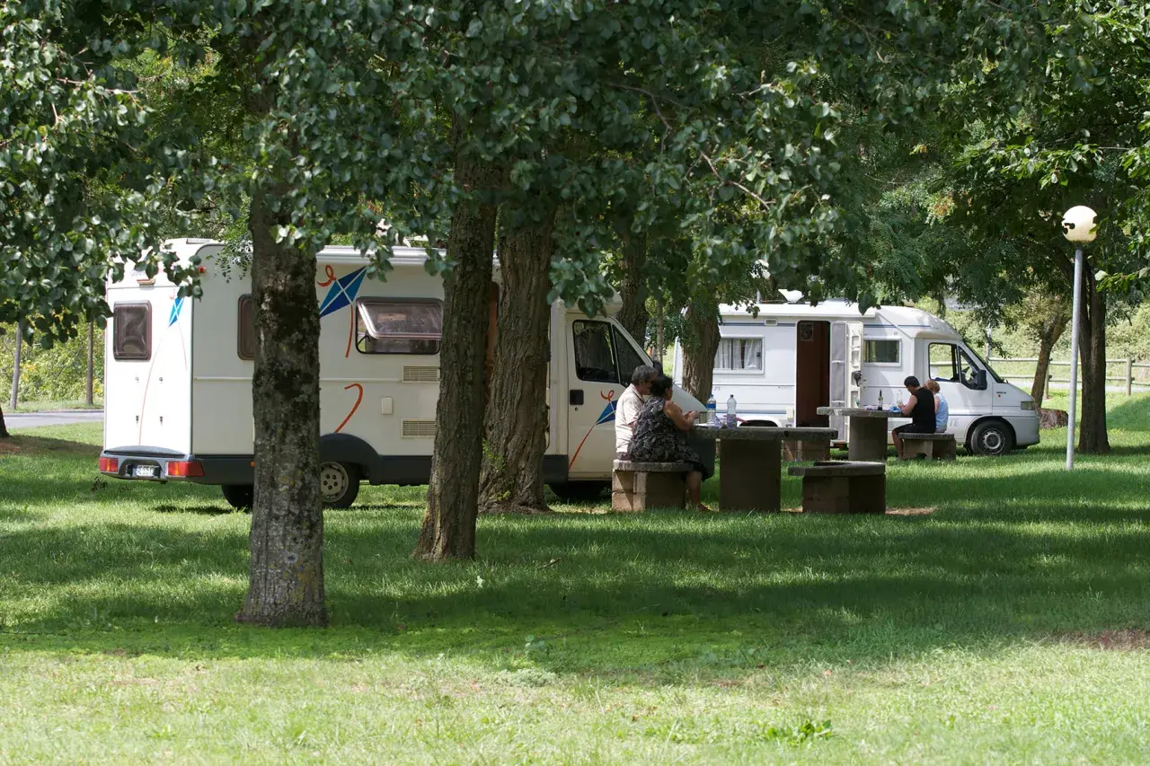 Des camping-cars stationnés dans un parc ombragé, des gens profitent de pique-niques. Un aperçu des plus belles aires de camping-car gratuites.