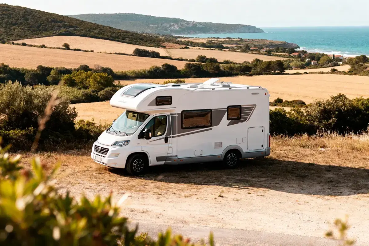 Camping-car blanc prêt pour une idée sortie week-end. Paysage de champs dorés et mer bleue en arrière-plan.
