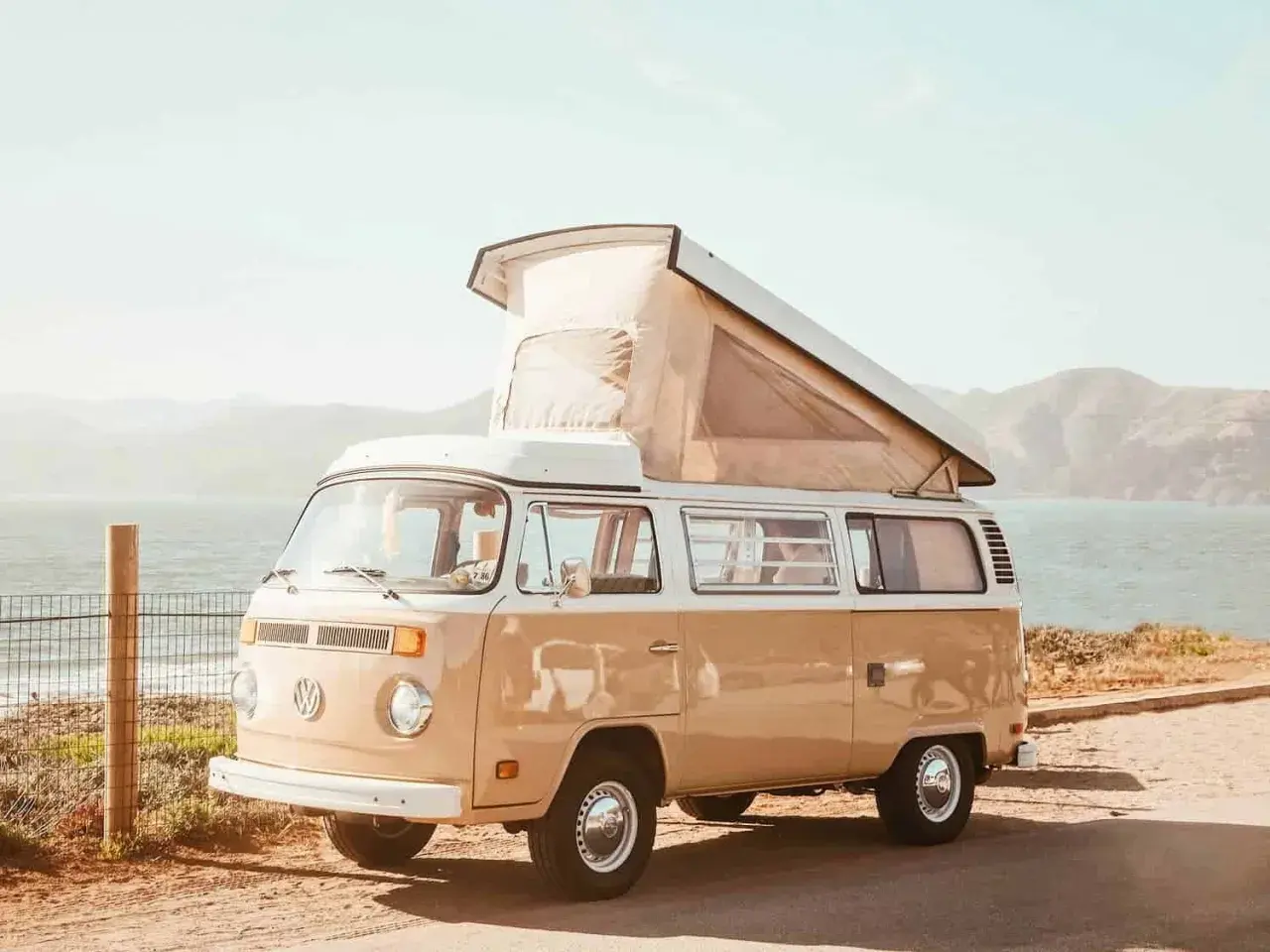 Un camping-car Volkswagen vintage, prêt pour l'aventure, avec son toit relevé, face à la mer et aux collines. L'esprit des 5 Terres en camping-car.