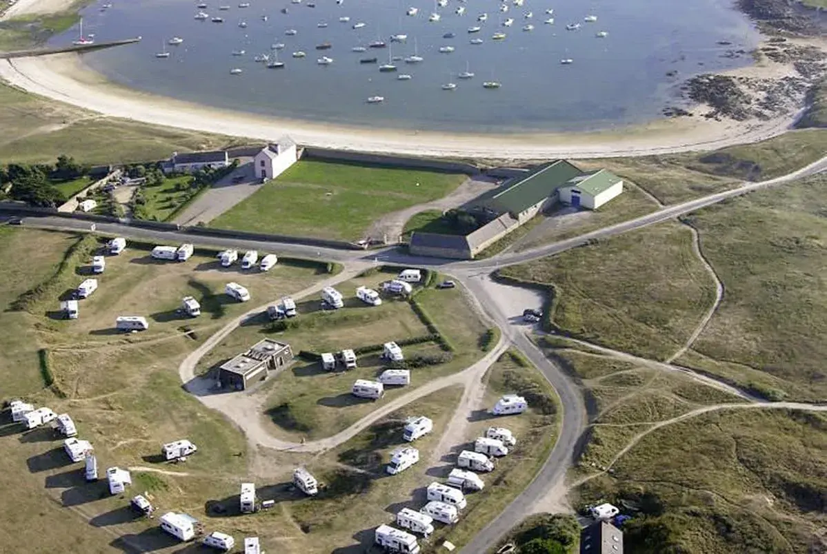 Vue aérienne d'une aire de camping-car finistère gratuit, avec des caravanes garées près d'une baie bordée de bateaux.