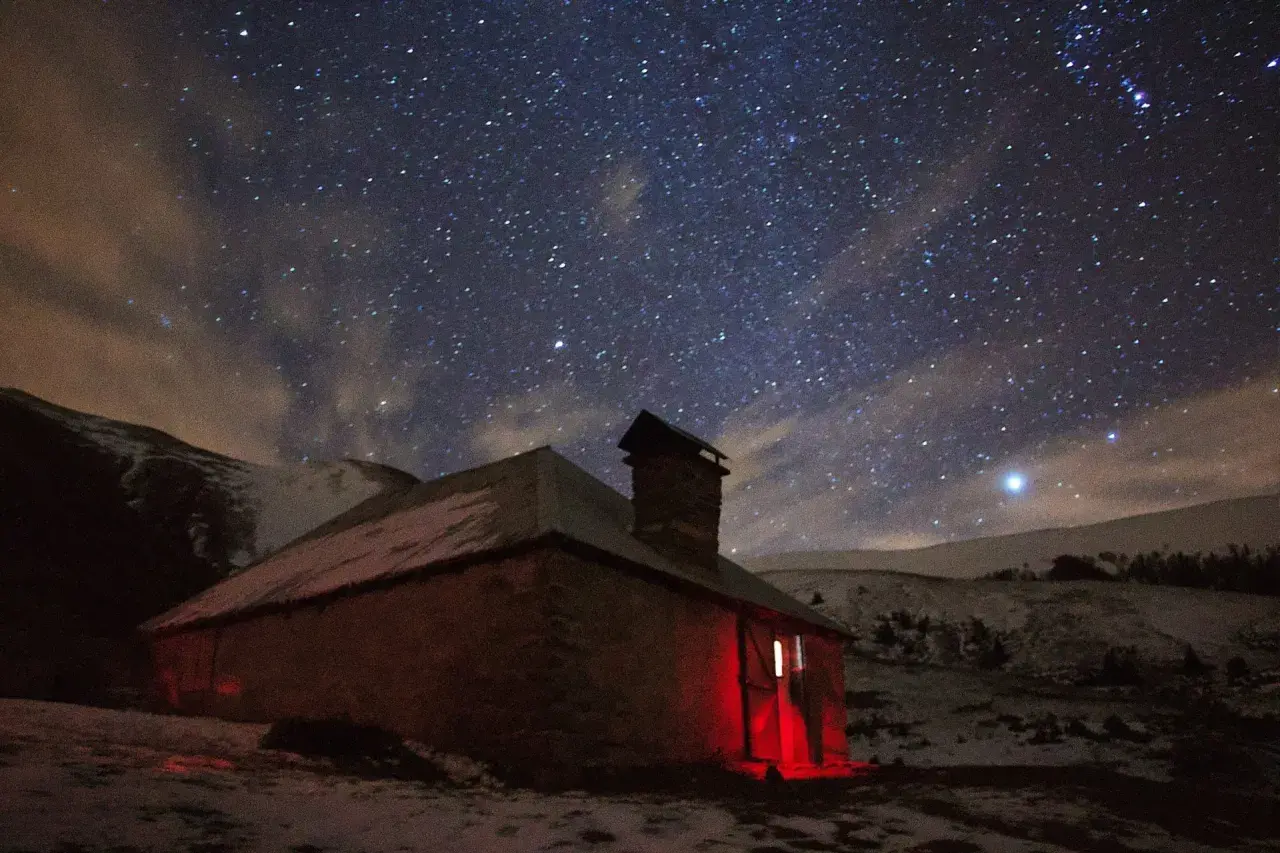 Un refuge illuminé par une lumière rouge sous un ciel étoilé. L'endroit parfait pour dormir en refuge après une longue journée.