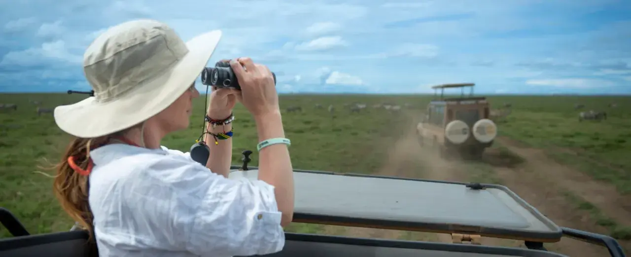 Une femme en safari, jumelles à la main, observe des zèbres en Tanzanie. Une excellente idée de que faire en Tanzanie !