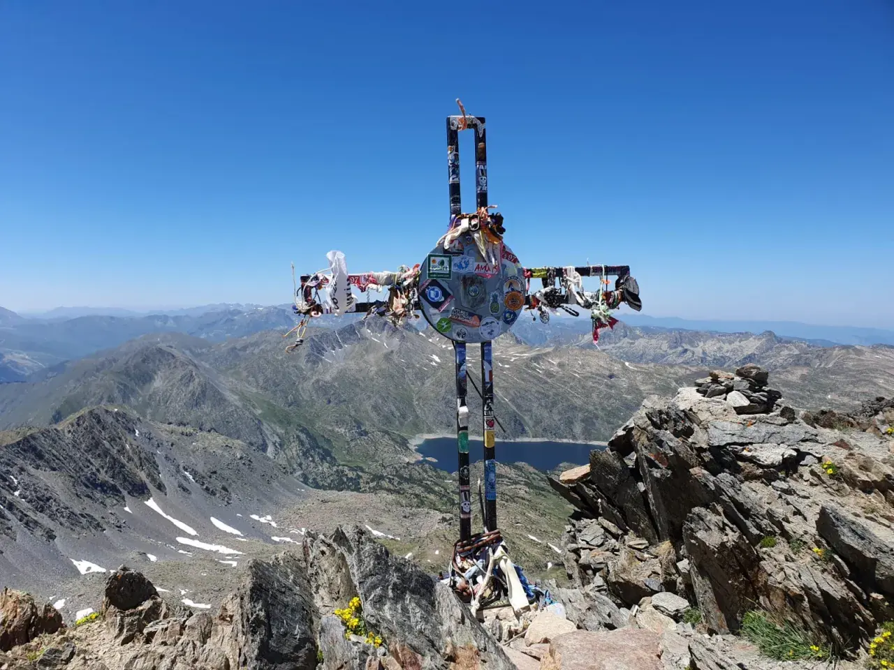 Croix ornée de souvenirs, au sommet d'une montagne, témoin d'un carlit randonnée mémorable. Paysage de haute altitude sous un ciel bleu.
