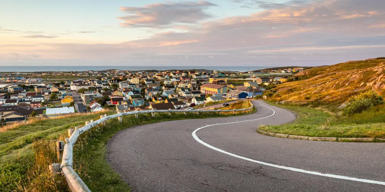 Vue panoramique de Saint-Pierre-et-Miquelon, avec ses maisons colorées nichées sur la côte et une route sinueuse menant au village.