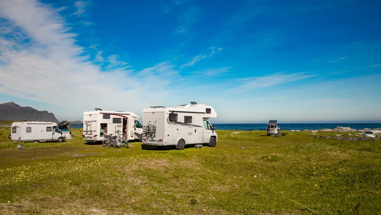 Plusieurs camping-cars stationnés sur une aire de camping car gratuite, face à la mer sous un ciel bleu.
