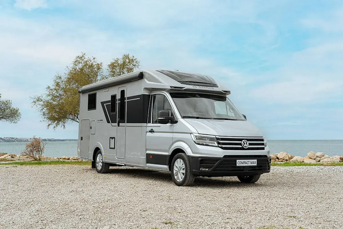 Camping car petite taille Adria Compact Max argenté, garé sur un chemin de gravier près de la mer.