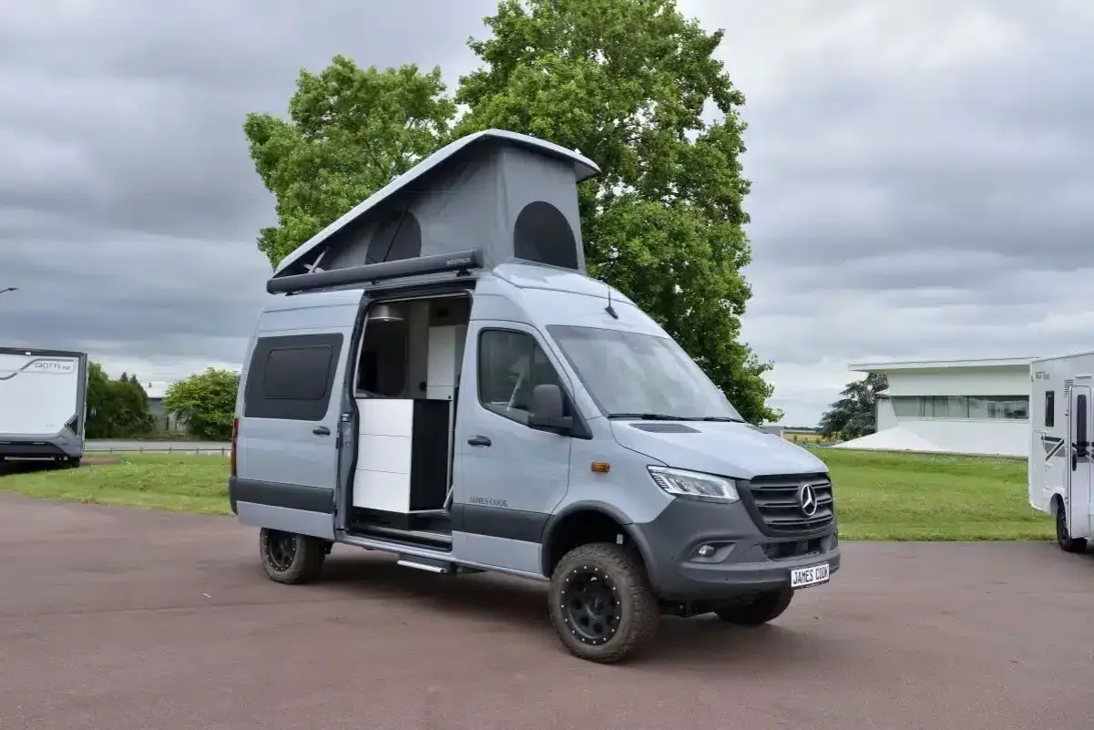 Camping car 4x4 gris avec toit relevable ouvert, prêt pour l'aventure.