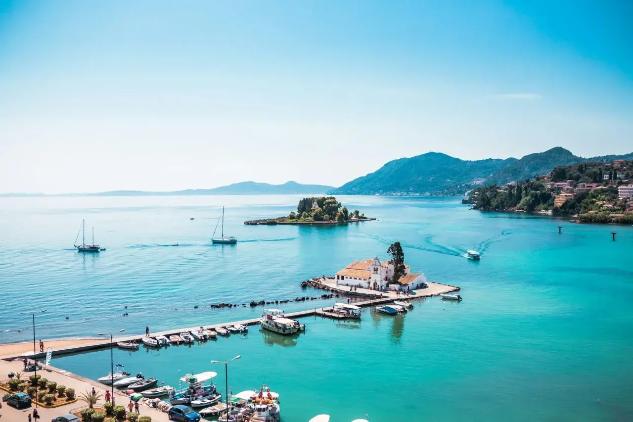 Vue idyllique de la baie de Corfou avec des bateaux, une église sur un îlot et des collines verdoyantes. Idéal pour savoir que faire à Corfou.