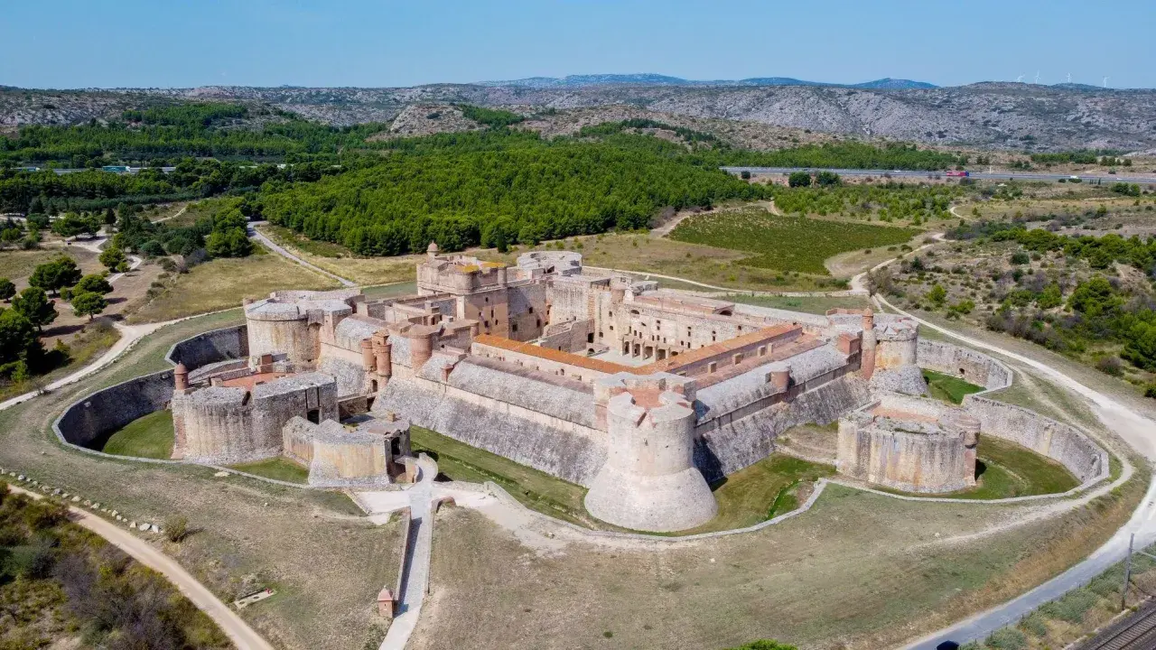 Vue aérienne du Fort de Salses, une imposante citadelle sur la côte vermeille, entourée de verdure et de collines.