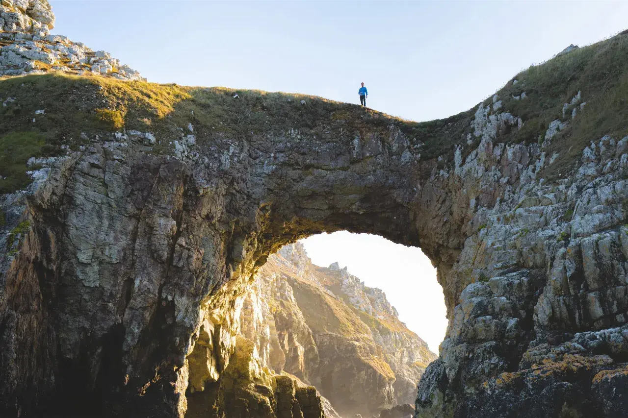 Un homme seul au sommet de la pointe de Dinan, surplombant un arc rocheux naturel.