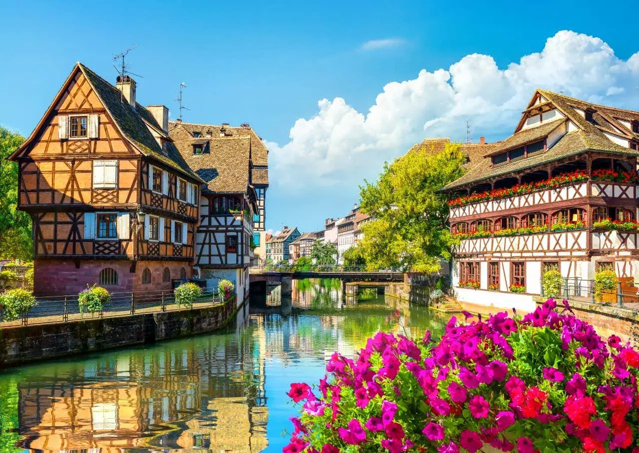 La Petite France à Strasbourg, un joyau pour l'alsace tourisme. Maisons à colombages pittoresques au bord de l'eau, reflets dans le canal, fleurs éclatantes.